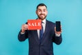 Satisfied cheerful businessman in suit holding smartphone with blank display and sale card in hands Royalty Free Stock Photo