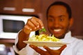 Satisfied chef wearing white clothes placing green leaf on top of spaghetti dish, smiling happily holding plate up in Royalty Free Stock Photo