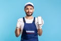 Satisfied consultant in overalls and gloves holding mobile phone with mock up display and showing thumbs up