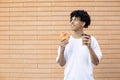 Satisfied curly-haired American guy holding an orange donut and a cup of coffee, looking at copy space Royalty Free Stock Photo