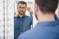 Satisfied Customer. View of happy young male client wearing new glasses, standing near rack and showcase with eyewear Royalty Free Stock Photo