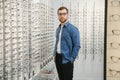 Satisfied Customer. View of happy young male client wearing new glasses, standing near rack and showcase with eyewear Royalty Free Stock Photo