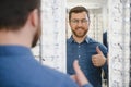 Satisfied Customer. View of happy young male client wearing new glasses, standing near rack and showcase with eyewear Royalty Free Stock Photo