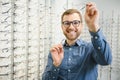 Satisfied Customer. View of happy young male client wearing new glasses, standing near rack and showcase with eyewear Royalty Free Stock Photo