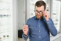 Satisfied Customer. View of happy young male client wearing new glasses, standing near rack and showcase with eyewear Royalty Free Stock Photo