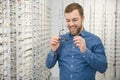 Satisfied Customer. View of happy young male client wearing new glasses, standing near rack and showcase with eyewear Royalty Free Stock Photo