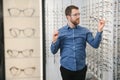 Satisfied Customer. View of happy young male client wearing new glasses, standing near rack and showcase with eyewear Royalty Free Stock Photo