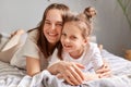Satisfied delighted mother embracing daughter in bedroom at home looking at camera with smiles spending lazy morning in bed having