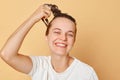 Satisfied delighted woman washes hair applies shampoo taking shower isolated over beige background looking at camera with toothy