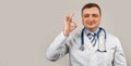 Satisfied doctor man in a medical coat and with a stethoscope shows okay okay sign of approval smiles, white background