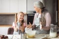 Satisfied european small granddaughter and mature grandmother in aprons make dough with flour, have fun together Royalty Free Stock Photo