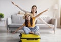 Satisfied excited chinese teenager girl, young mother spread arms to sides like airplane and sit on yellow suitcase