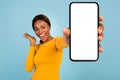 Satisfied excited pretty young african american female in yellow t-shirt show smartphone with blank screen