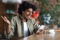 Satisfied excited surprised curly young black guy rejoices to victory and looks at smartphone