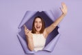 Satisfied excited young brunette woman in casual clothing breaking through purple paper hole betting and winning holding Royalty Free Stock Photo