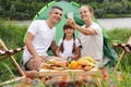 Satisfied family woman man and little girl sitting near tent having picnic by the river enjoying nature mother making selfie via Royalty Free Stock Photo