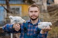A satisfied farmer portrait of Caucasian a man with a beard, in overalls and a shirt, holds two white dwarf chickens in his arms Royalty Free Stock Photo
