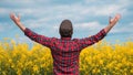 Satisfied farmer raising hands in blooming canola rapeseed field, rear view Royalty Free Stock Photo