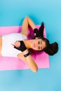 A satisfied girl after fitness exercises lies on the mat and looks at her result on a fitness watch. Blue background