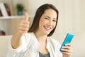 Satisfied girl holding smart phone with thumbs up