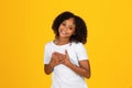 Satisfied glad curly teenager black girl in white t-shirt presses hands to chest, says thank