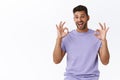 Satisfied handsome bearded millennial guy in purple t-shirt, showing okay gesture, express delighted, overjoy of good