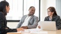 A satisfied African American businessman discussing work with Asian female assistants in the meeting Royalty Free Stock Photo