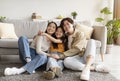 Satisfied happy chinese teen daughter in casual clothes hugs young parents, sitting on floor in living room