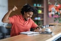 Satisfied happy excited millennial african american curly man rejoices to victory and excellent result at table