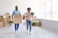 Satisfied happy millennial african american male and female carry cardboard boxes with belongings in empty room