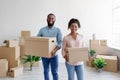 Satisfied happy young african american husband and wife carry boxes with belongings in new flat