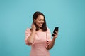 Satisfied lovely woman with dark hair in pink dress holds cell phone in hand, texts friend in chat, smiles broadly Royalty Free Stock Photo