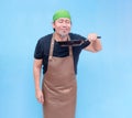 A satisfied middle-aged barista raising a frying pan near his face to smell it with his eyes closed. Isolated on a blue background