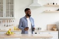 Satisfied millennial african american male with beard enjoys morning and drink in cup with smartphone
