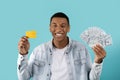 Satisfied millennial black man show dollars, credit card, rejoice to victory online, recommends savings