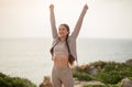 Satisfied millennial caucasian lady athlete in sportswear raises hands up, celebrates win, workout result, success