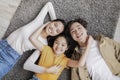 Satisfied millennial japanese mother, father and teen daughter lie on floor on gray carpet in room interior