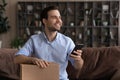 Satisfied millennial man sit on couch hold postal parcel smartphone