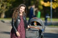 Satisfied mom on a walk with a stroller. Young mother walking with baby in the park. Beautiful smile and uplifted mood, satisfied