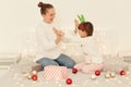 Satisfied mother and daughter wearing casual style white sweaters sitting on bed holding each other hands, celebrating winter Royalty Free Stock Photo