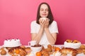 Satisfied overjoyed calm brown haired woman in white t shirt sitting at table with pastry smelling pleasant aromat of coffee or