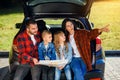 Satisfied family of handsome father, pretty mother and lovely kids which are looking on the road map while sitting in Royalty Free Stock Photo