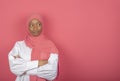 Satisfied religious female model has arms folded, looks aside, wears pink headscarf standing on pink background, copy space for