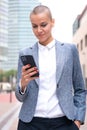 Vertical portrait caucasian business woman using an app on her smartphone outdoors. Royalty Free Stock Photo