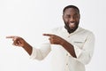 Satisfied successful and happy dark-skinned male model with beard and short haircut in white formal shirt pointing with