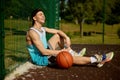 Satisfied teenage basketball player rest sitting on street court