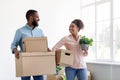 Satisfied young african american family look at each other and hold cardboard boxes, potted plants Royalty Free Stock Photo