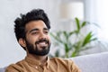 Satisfied young Indian man sitting on sofa at home and resting. Smiling man looks to the side, close-up photo Royalty Free Stock Photo