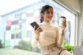 Satisfied young woman enjoy her morning coffee and using on smartphone near window Royalty Free Stock Photo