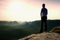 Satisfy tall hiker in grey shirt and dark trousers. Sprtsman on the peak of sharp rock edge watching down to landscape.